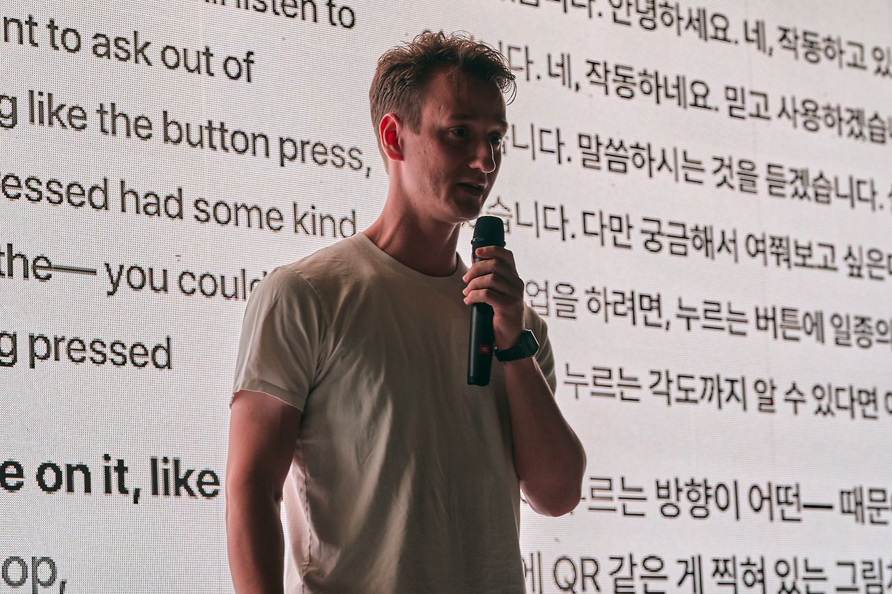 Miodrag holding a microphone, pitching his robot idea in front of a screen of live English and Korean captions.